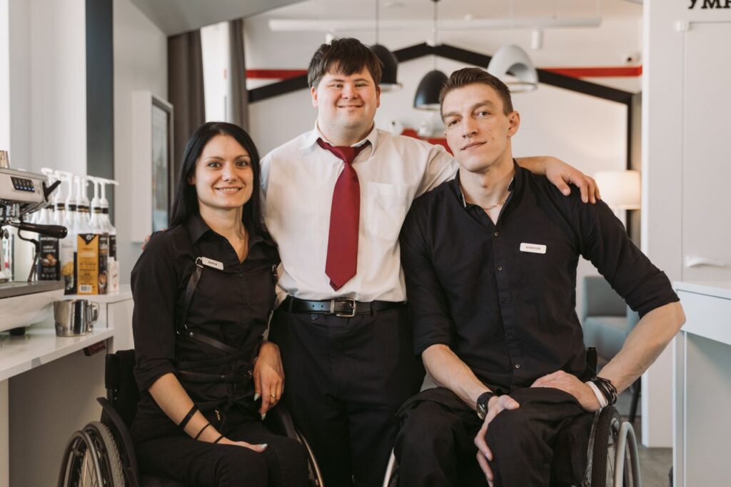 disabled supporting independent living each other A group of diverse adults, including those in wheelchairs, smiling in a cafe environment fostering teamwork.